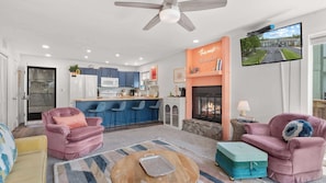 A modern living room with a fireplace, a television, and a kitchen area. - Daylight Cove Lakefront Chic (Lake Ozark)