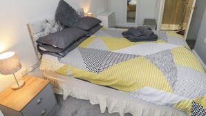 A neatly made bed with a patterned bedspread, a bedside lamp, a wooden nightstand, a grey drawer unit, and a wardrobe with a mirror. - The Annex at Ryefield Lodge (Holmfirth)