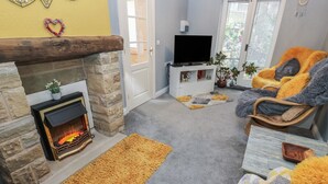 A cozy living room with a stone fireplace, a flat-screen TV, a comfortable chair, and a small white cabinet. - The Annex at Ryefield Lodge (Holmfirth)
