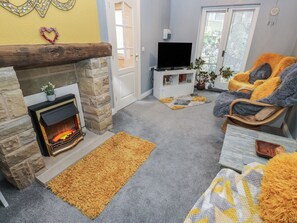 A cozy living room with a stone fireplace, a flat-screen TV, a comfortable chair, and a small white cabinet. - The Annex at Ryefield Lodge (Holmfirth)