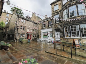 A traditional stone building with a cafe and deli signs, outdoor seating, and a wet pavement. - The Annex at Ryefield Lodge (Holmfirth)