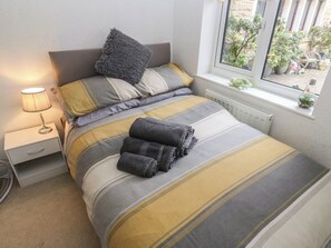 A neatly made bed with striped bedding, a bedside lamp, and a window with a view of the outside. - The Annex at Ryefield Lodge (Holmfirth)