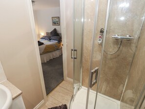 A bathroom with a shower, toilet, and a bed in the adjacent room. - The Annex at Ryefield Lodge (Holmfirth)