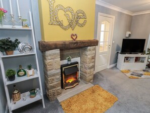 A living room with a fireplace, a bookshelf, a TV stand, and a 'Love' decoration on the wall. - The Annex at Ryefield Lodge (Holmfirth)