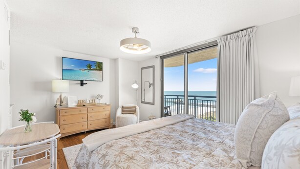 Une chambre avec un lit, un bureau, une chaise, une commode, une télévision et un balcon donnant sur la mer.