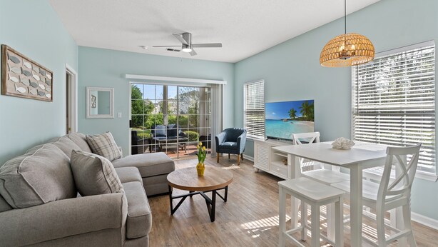 A living room with a sofa, coffee table, TV, and dining table. - Cross Gate 104 - End Unit, Lake View, Pool (Surfside)