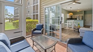 A covered patio with wicker furniture, a sliding glass door leading to a kitchen, and a view of neighboring houses. - Cross Gate 104 - End Unit, Lake View, Pool (Surfside)