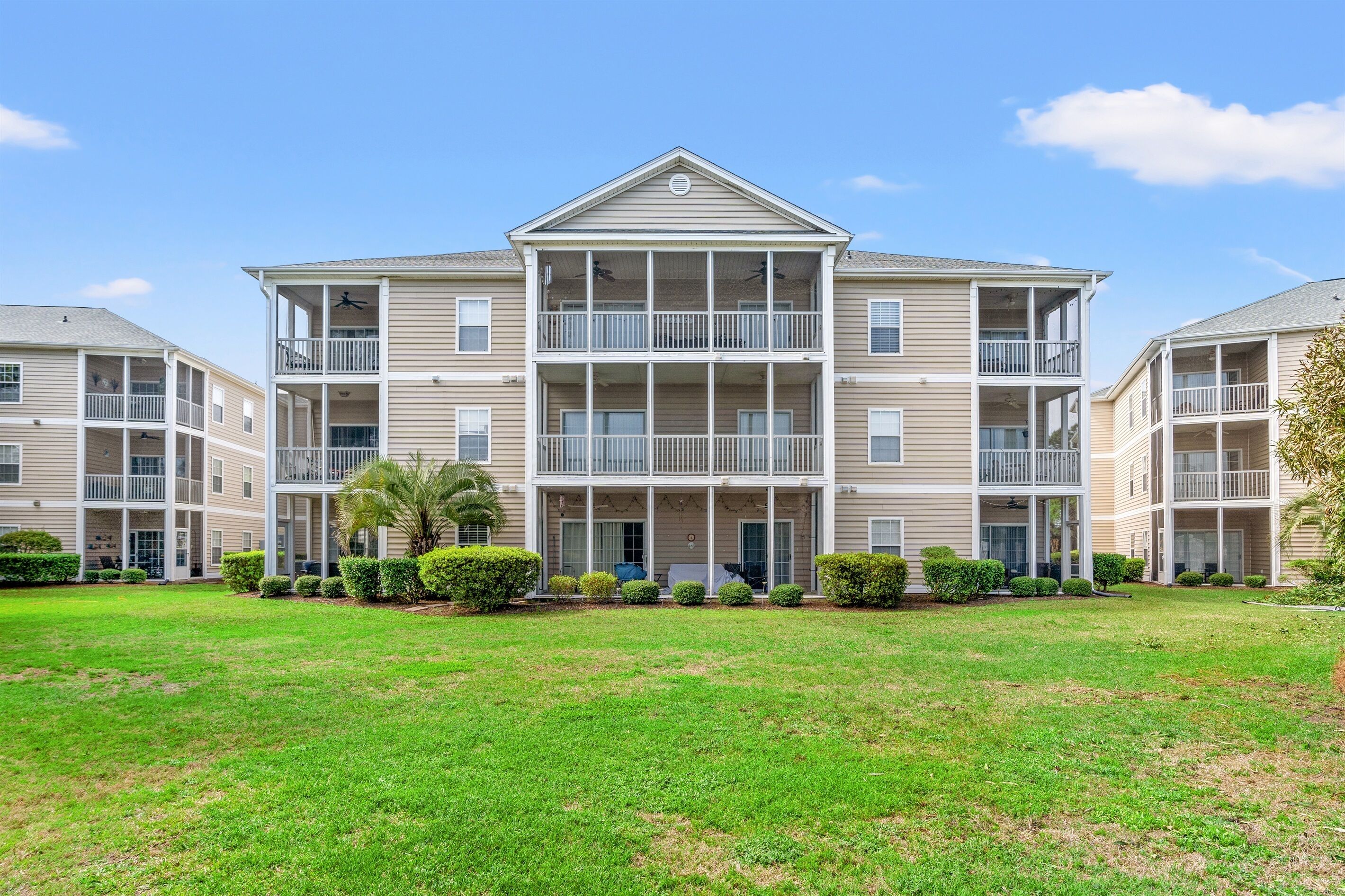 A multi-story residential building with balconies, a central entrance, and a well-maintained lawn.
