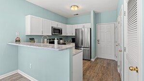 A kitchen with white cabinets, stainless steel appliances, and a marble countertop. - Cross Gate 104 - End Unit, Lake View, Pool (Surfside)