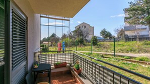 Een balkon met een tafel en stoelen, planten in potten en uitzicht op een gebouw en groen.