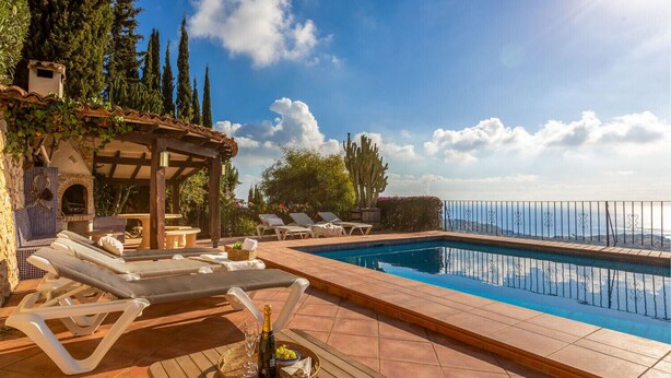 Area piscina con lettini, un tavolo con una bottiglia e degli acini d'uva, e vista sul mare.