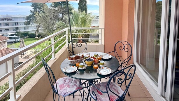 A balcony with a table set for breakfast, chairs, and a large umbrella. - Sea view, Terrace Secured parking near beach railway station and park (Villeneuve-Loubet)