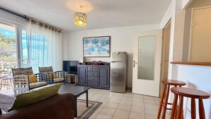 A modern living room with a sofa, chairs, a television, a kitchen area with a refrigerator, and a dining area with stools. - Sea view, Terrace Secured parking near beach railway station and park (Villeneuve-Loubet)