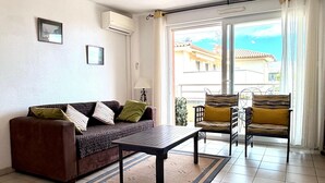 A living room with a sofa, a coffee table, and two chairs. There is a window with curtains, a ceiling light, and a picture frame on the wall. - Sea view, Terrace Secured parking near beach railway station and park (Villeneuve-Loubet)