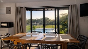 A dining area with a table and chairs, a television, and a view of a swimming pool and greenery. - Villa 3 bedrooms / 3 bathrooms • Private swimming pool - Tamarindo (Tamarindo)