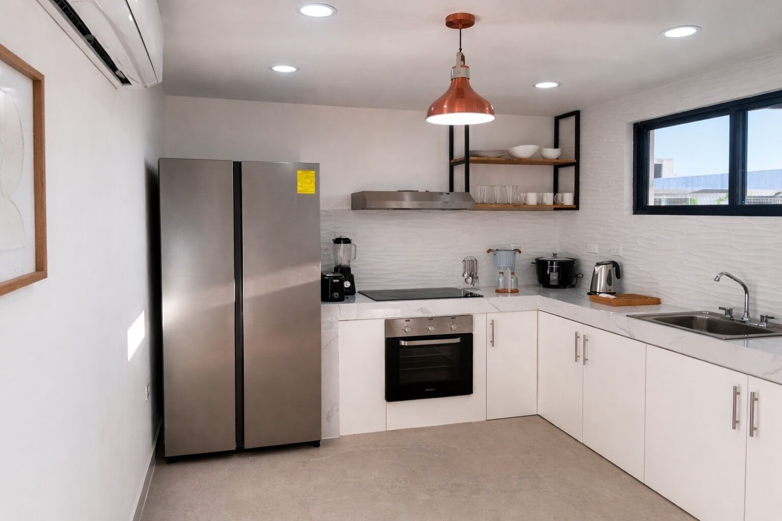 A modern kitchen with a stainless steel refrigerator, a built-in oven, a coffee maker, and a window providing a view.