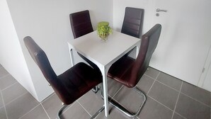 A dining area with a white table, four dark chairs, and a green vase on the table.
