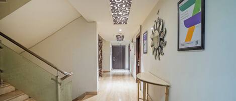 A hallway with a marble floor, a staircase with a metal handrail, and a wall with framed artwork.