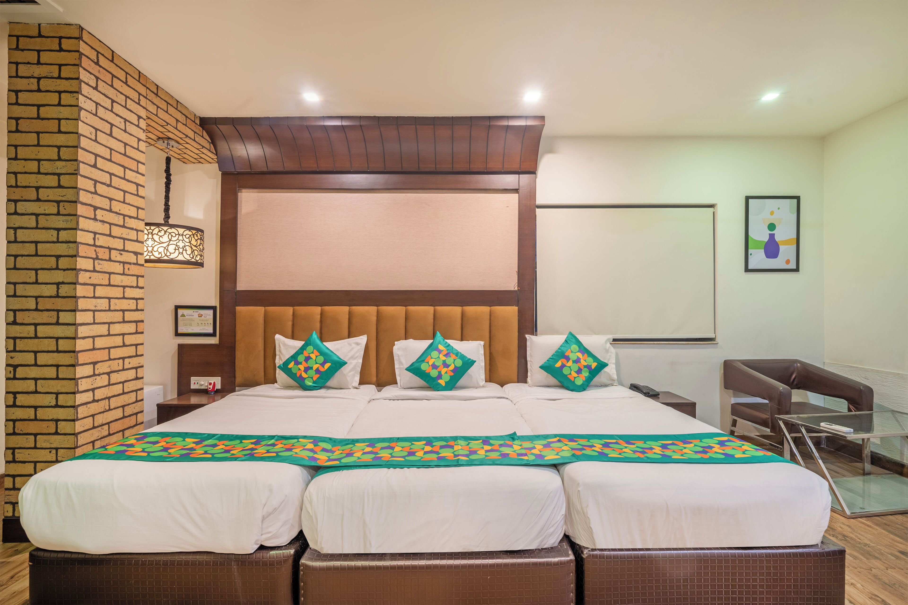 A hotel room with a large bed, a brick wall, a wooden headboard, and a glass table.