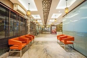 Un vestíbulo de hotel con piso de mármol, asientos naranja y un techo decorativo.