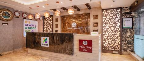 A hotel reception area with a marble floor, a reception desk, and a wall clock.