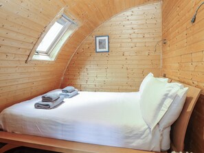 Ein Einzelbett mit weißer Bettwäsche, ein kleines Fenster und ein gerahmtes Bild an der Wand.