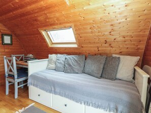 Une chambre mansardée chaleureuse avec un plafond en pente, une lucarne, un lit recouvert d’une couverture grise, une chaise et un petit bureau.