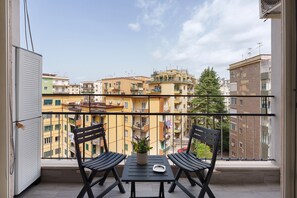 A balcony with a table and chairs, a potted plant, and a view of multi-story buildings. - Antonio's Home: Pet-Friendly Retreat (Napoli)