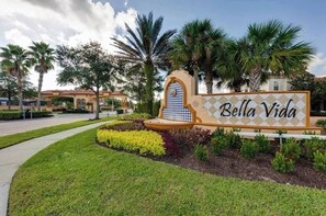 A sign for Bella Vida with a decorative archway and a well-maintained garden.