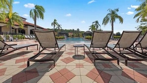 Un espace aménagé au bord de la piscine, avec des chaises longues, un sol carrelé et des palmiers.
