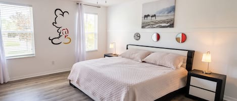 Quarto com cama, mesas de cabeceira, ventoinha no teto e obra de arte na parede.