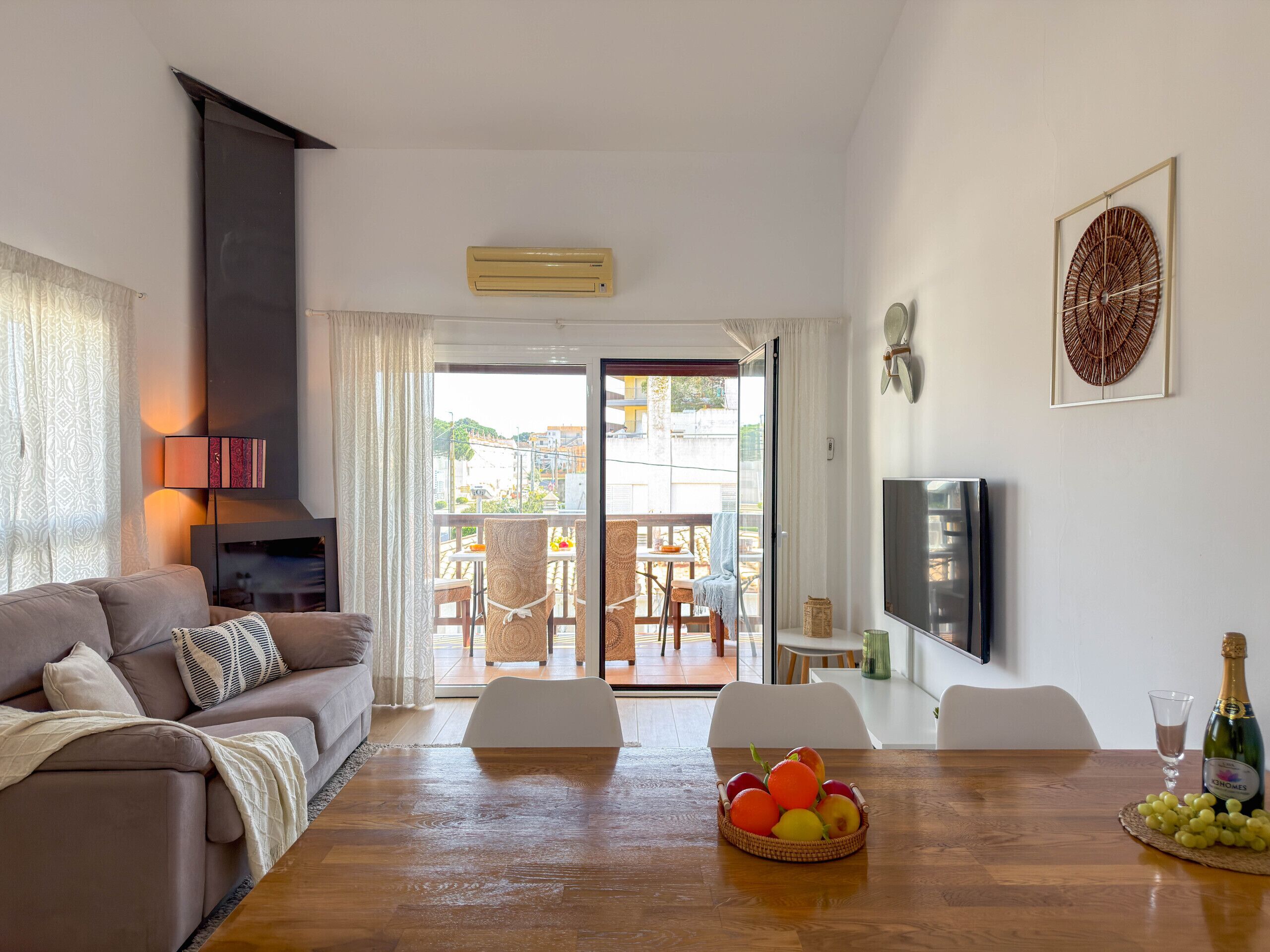 A living room with a sofa, a dining table with fruit, a TV, and a balcony with outdoor furniture.