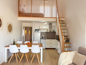 A modern apartment with a dining area, kitchen, and a loft bedroom with a wooden staircase. - Iona (L'Escala)