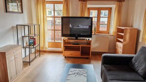 Een woonkamer met een televisie, een bank, een salontafel en een boekenkast.