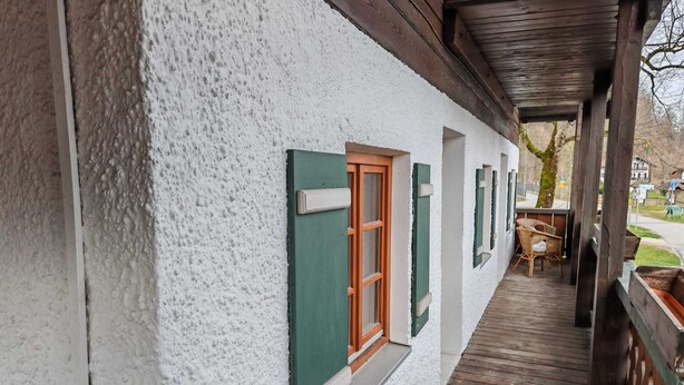 Een gebouw met een witte gevel, groene luiken en een houten terras.