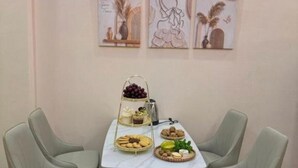 Spiseområde med et bord dækket til to, med et kagefad, kaffekande og en tallerken med småkager og ost.