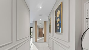 A hallway with white walls, a wooden door, and framed artwork on the walls. - Luxury Burj Royale 2BR Burj Khalifa & Fountain View With Balcony by Evoke (Dubai)