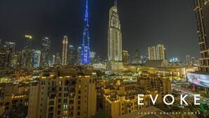 A cityscape at night with illuminated buildings, including a prominent tower with blue lights. - Luxury Burj Royale 2BR Burj Khalifa & Fountain View With Balcony by Evoke (Dubai)