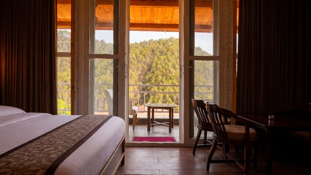 Une chambre dotée d’un grand lit, d’un bureau et d’une chaise, avec un balcon et une vue sur une forêt.