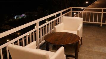 A balcony with white chairs and a round table, a white railing, and a view of the night sky.