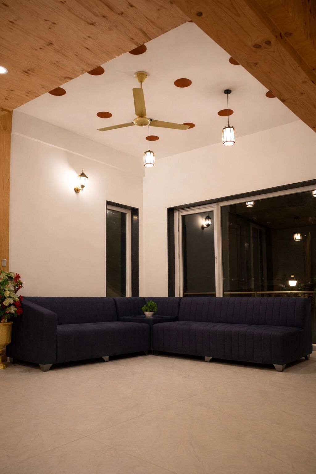 A modern living room with a dark blue sectional sofa, a ceiling fan, pendant lights, and large windows.