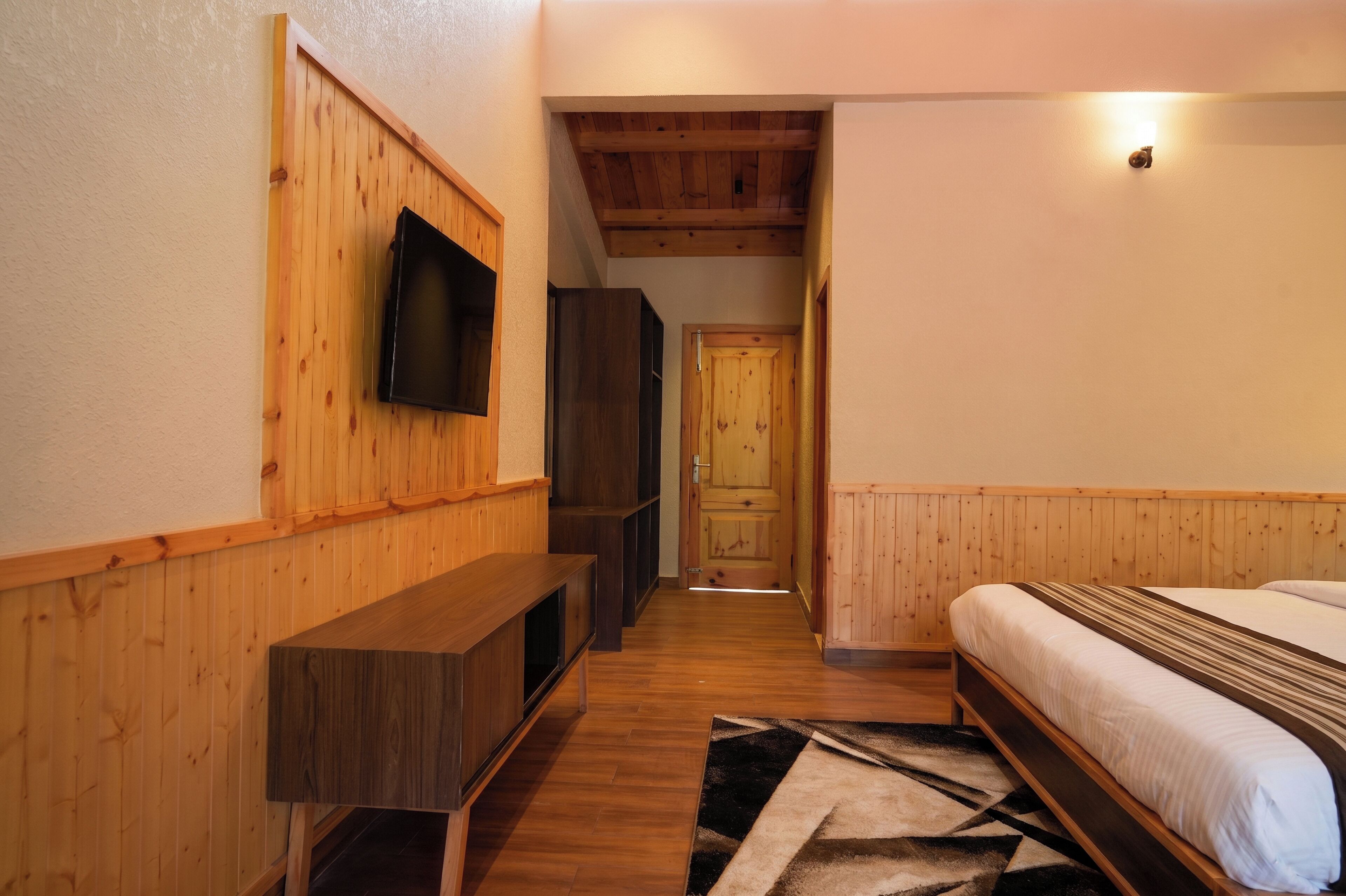 Een smalle gang met houten wanden, een bed met een gestreept dekbedovertrek, een wandtelevisie en een deur aan het einde.