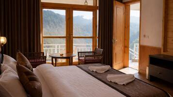 A hotel room with a bed, a table, two chairs, a desk, and a balcony with a mountain view.