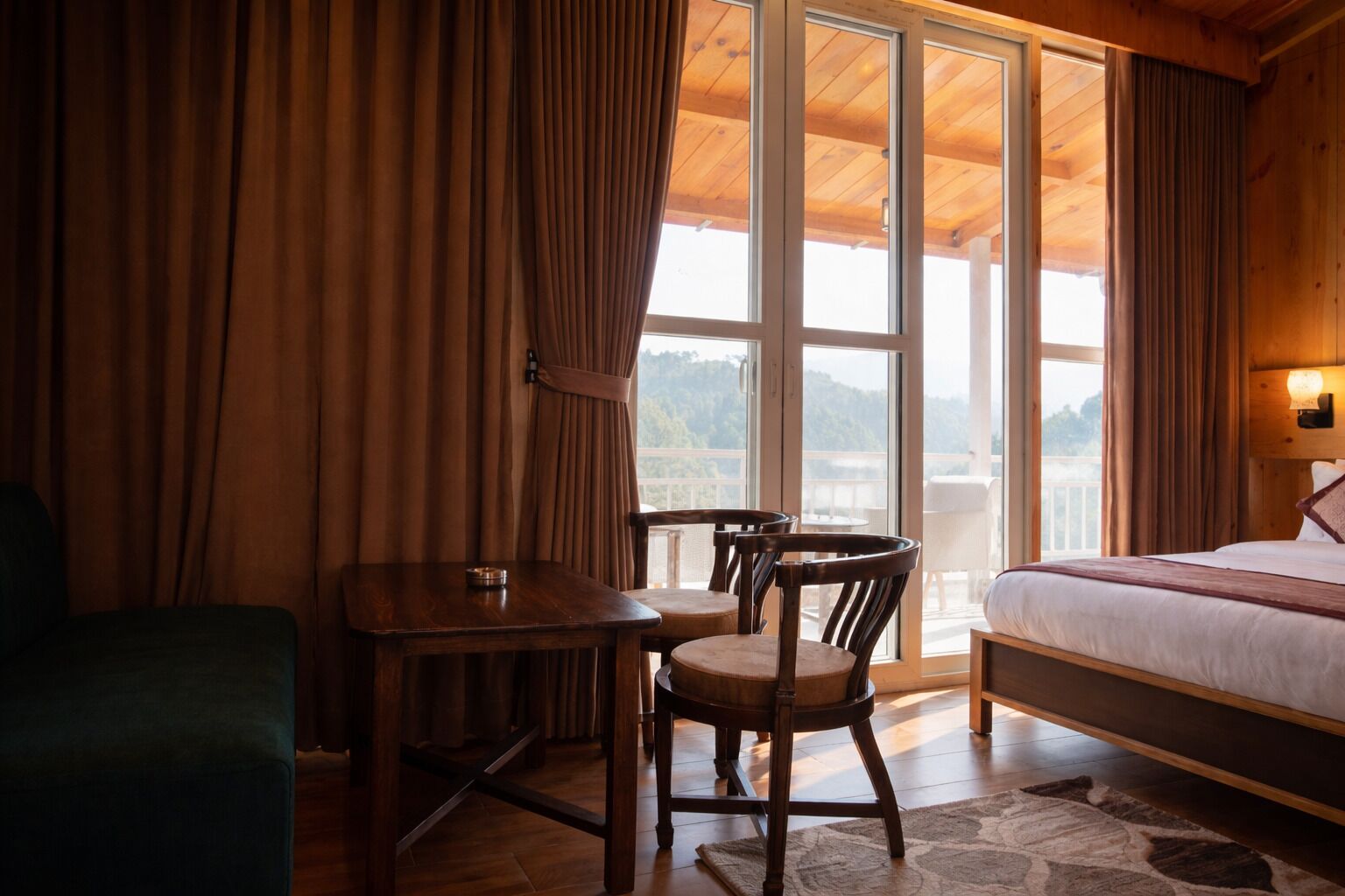 Ein Zimmer mit Bett, Tisch und Stühlen, Blick durch große Fenster und einer Holzbalkendecke.