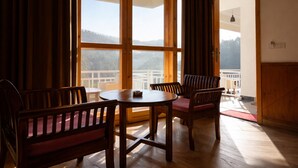 Une pièce avec une table et des chaises en bois, de grandes fenêtres avec des rideaux et une vue sur un balcon.