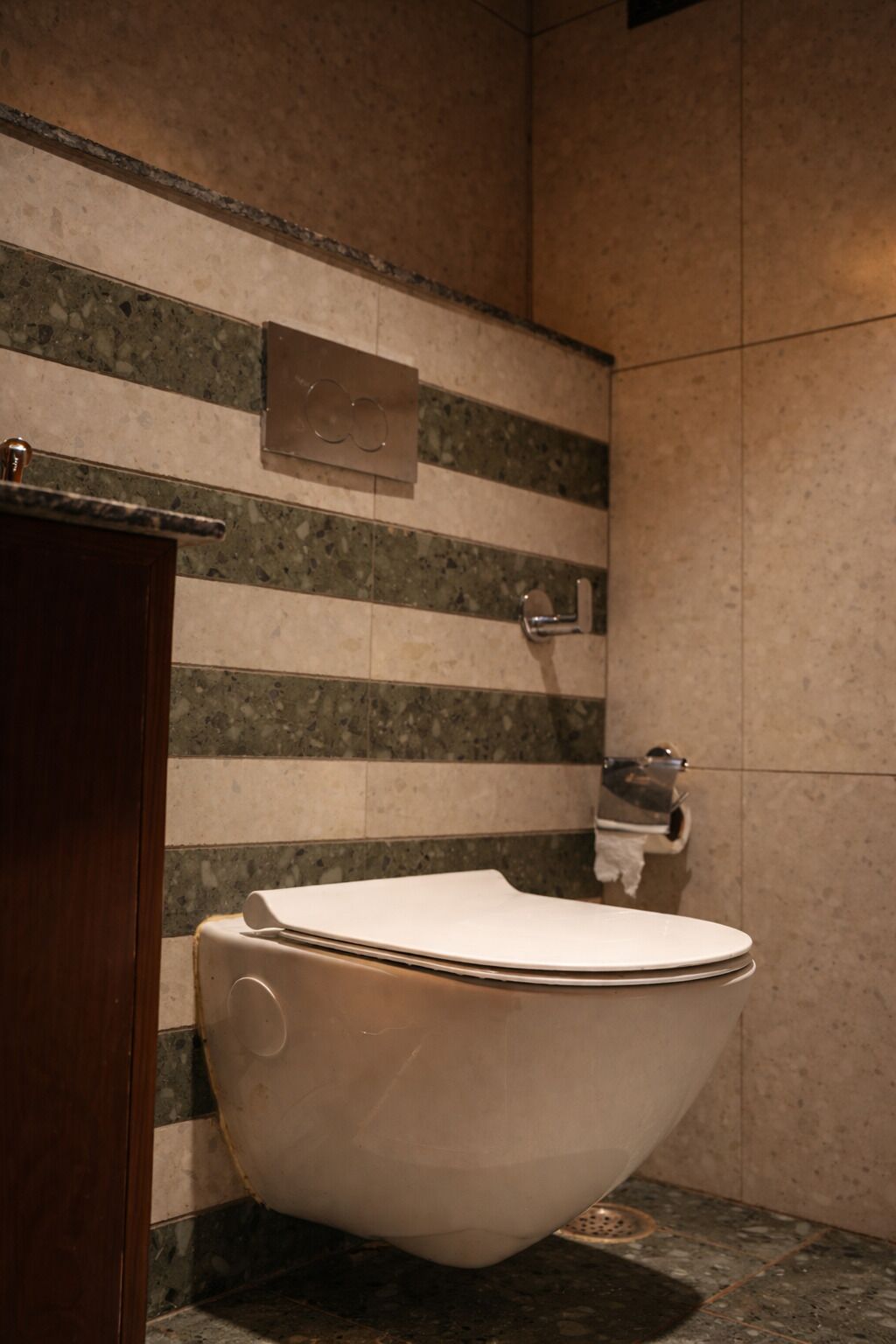 Un baño moderno con inodoro independiente, pared de mármol y mueble de madera.