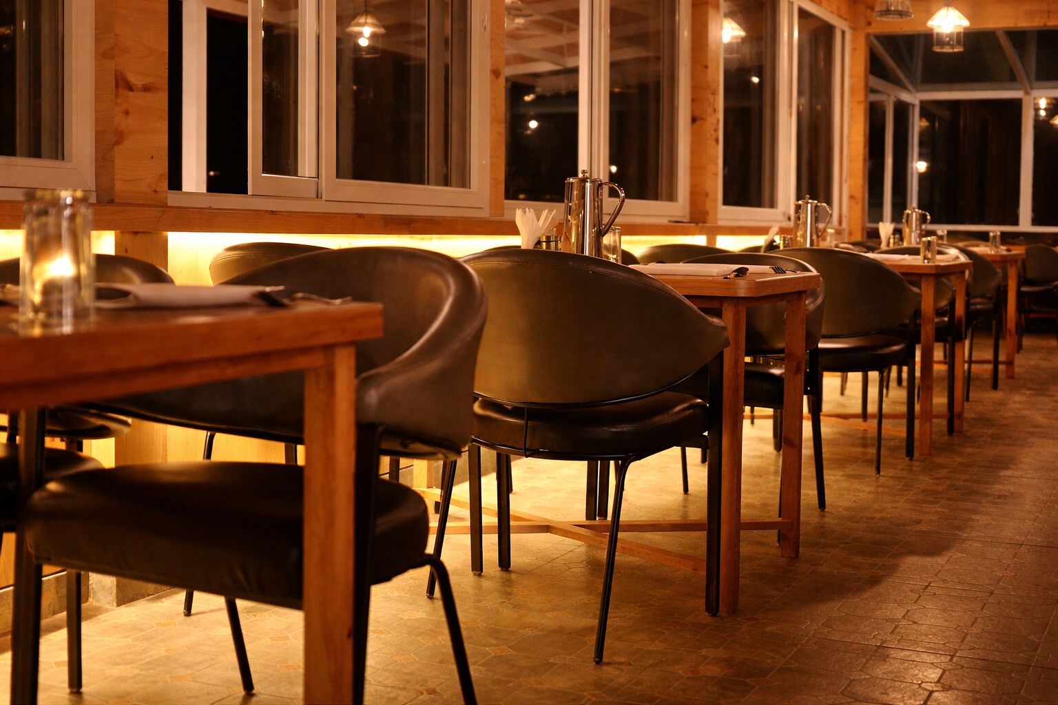 A restaurant with wooden tables and chairs, large windows, and a tiled floor.