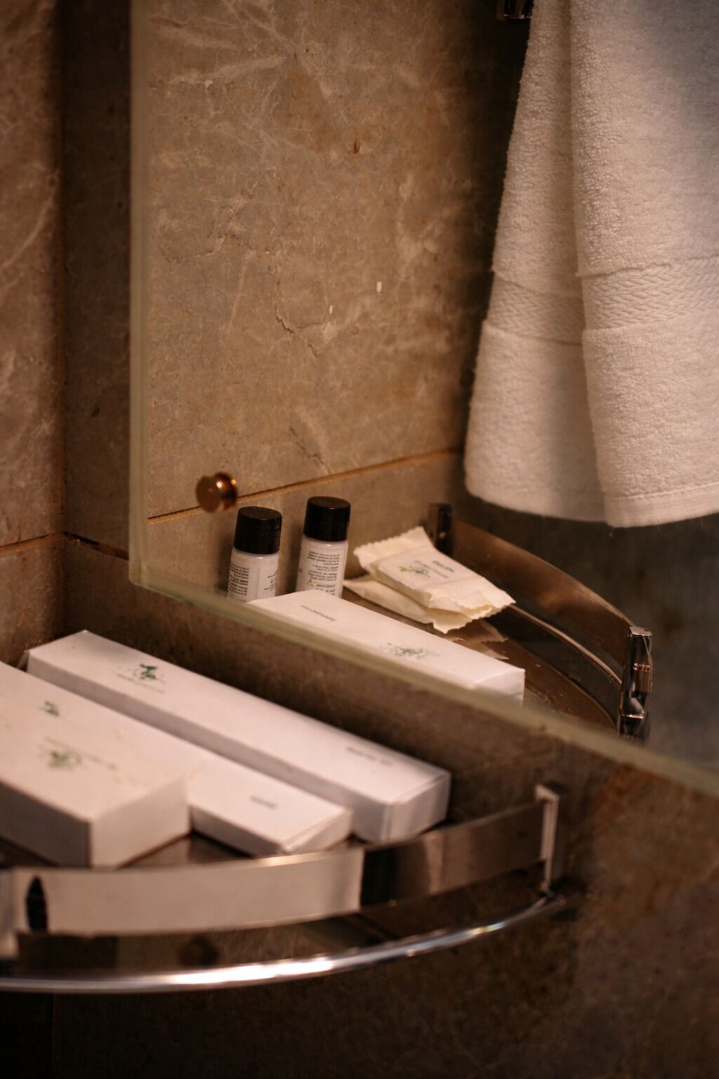 A bathroom with a marble wall, a sink with a mirror, and a towel rack.