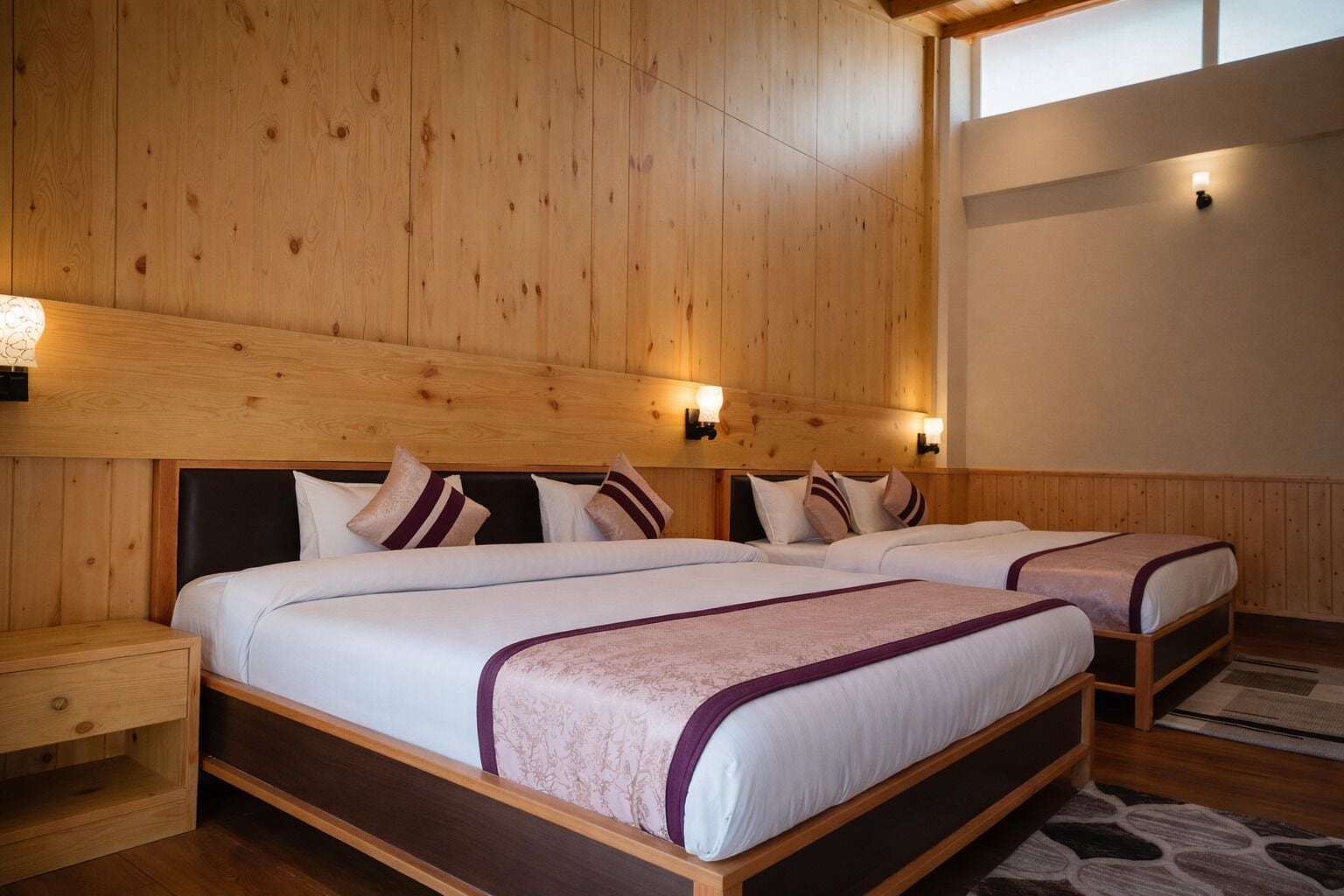 Quarto com painéis de madeira, duas camas, mesas de cabeceira e luminárias fixadas na parede.