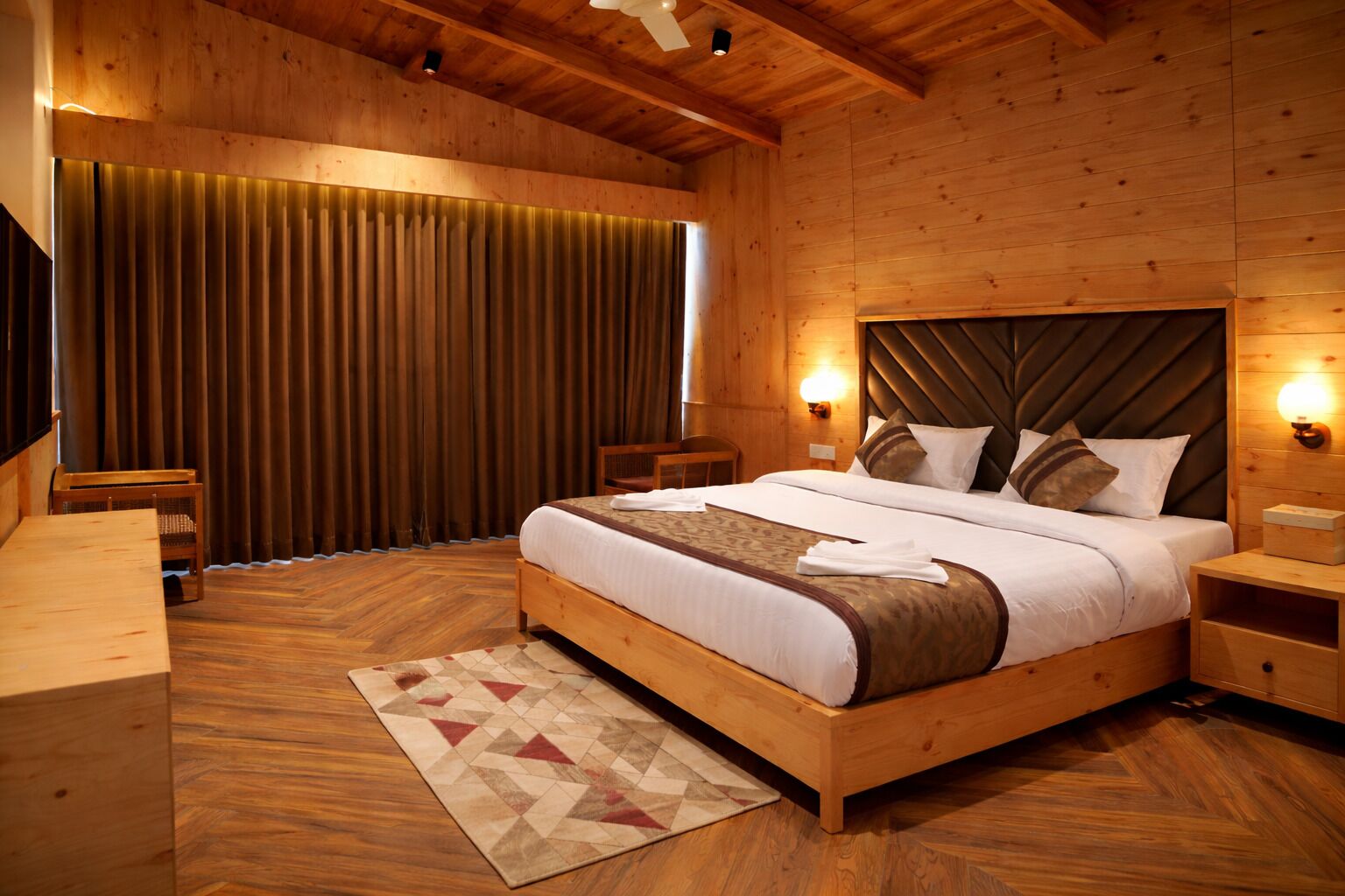 Ein Schlafzimmer mit Holzwänden, einem Bett, Nachttischen und einem großen Fenster mit Vorhängen.